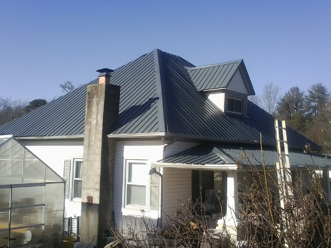 Dark blue standing seam metal roof on a white farmhouse with dormer — Slate & Tile Roof Repair by Roofing Brothers in Oostburg