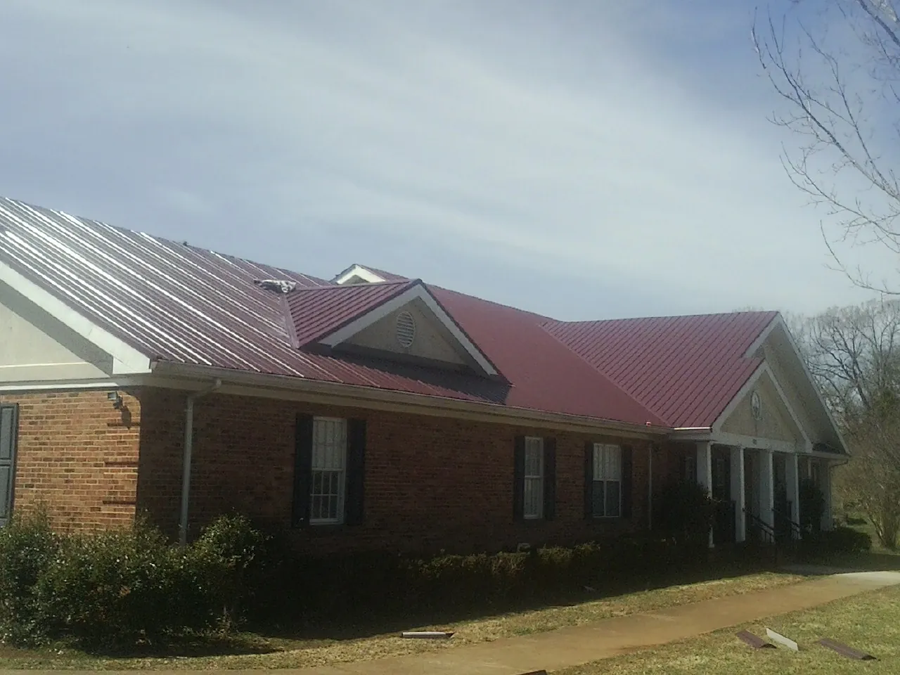Red metal roof with gabled entries on a long brick building, from a Hail Damage Roof Repair job in Oostburg