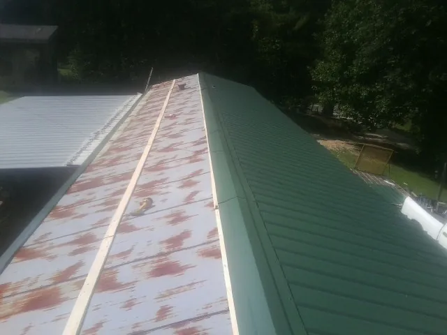 Old rusted panels beside newly installed green metal roofing — Wind Damage Roof Repair by Roofing Brothers in Oostburg