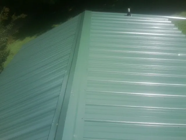 New green metal panels meeting at the ridge of a roof — Flat Roof Repair work by our crew in Oostburg