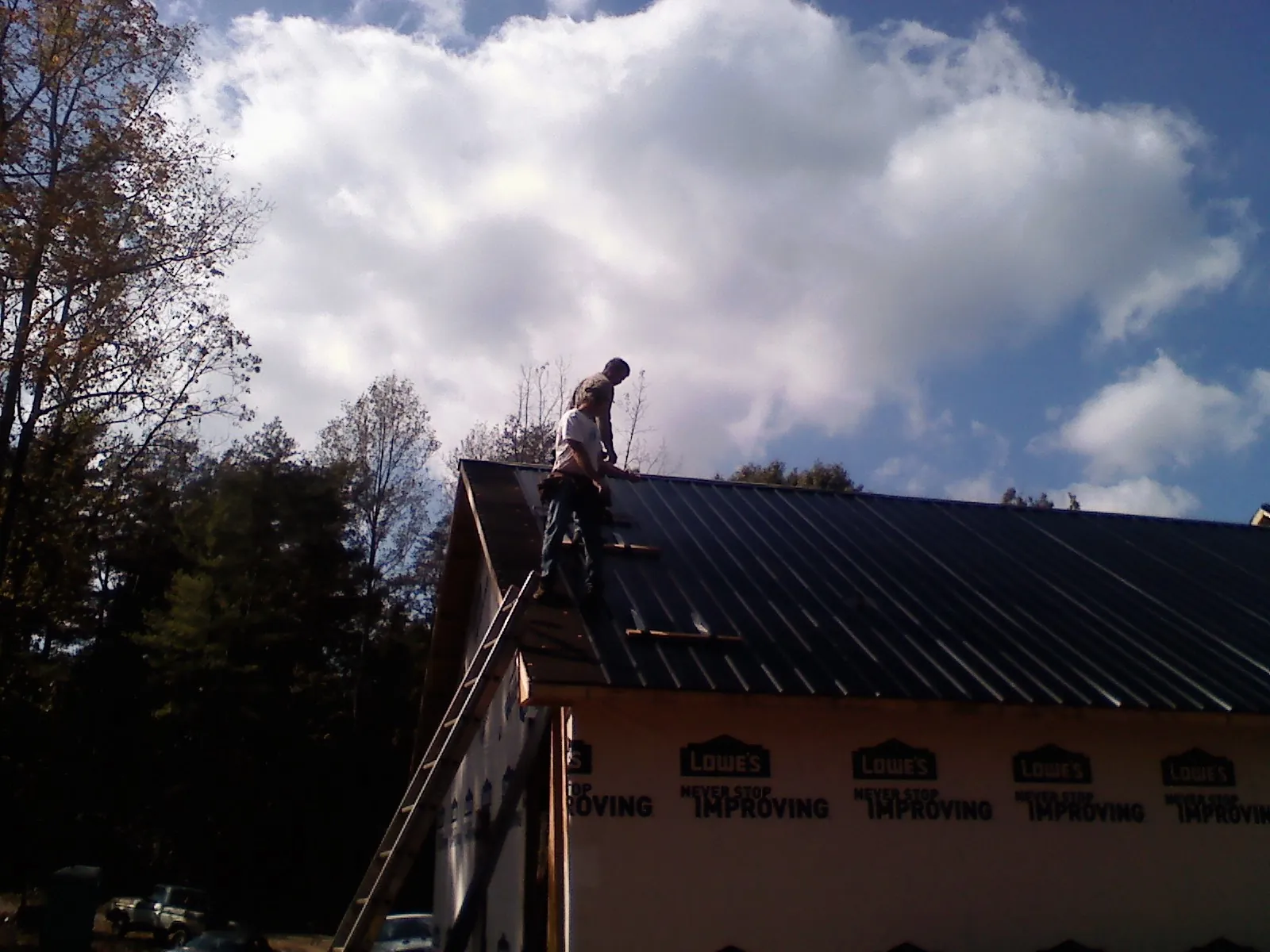 Roofer fastening dark metal panels high against a cloudy sky, from a Roof Inspection job in Oostburg