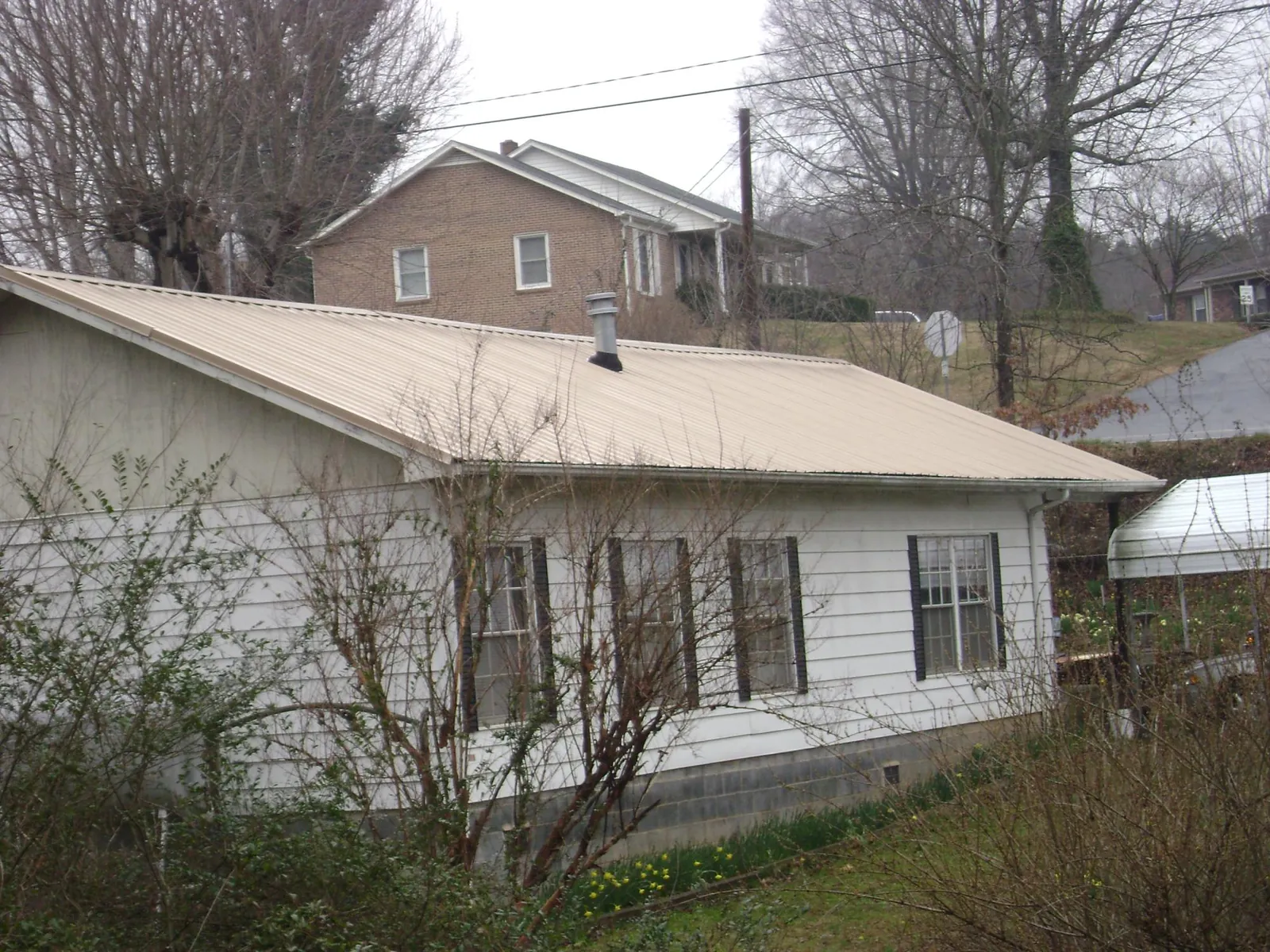 Tan metal roof on a white sided house set into a hillside — Commercial Roofing by Roofing Brothers in Oostburg