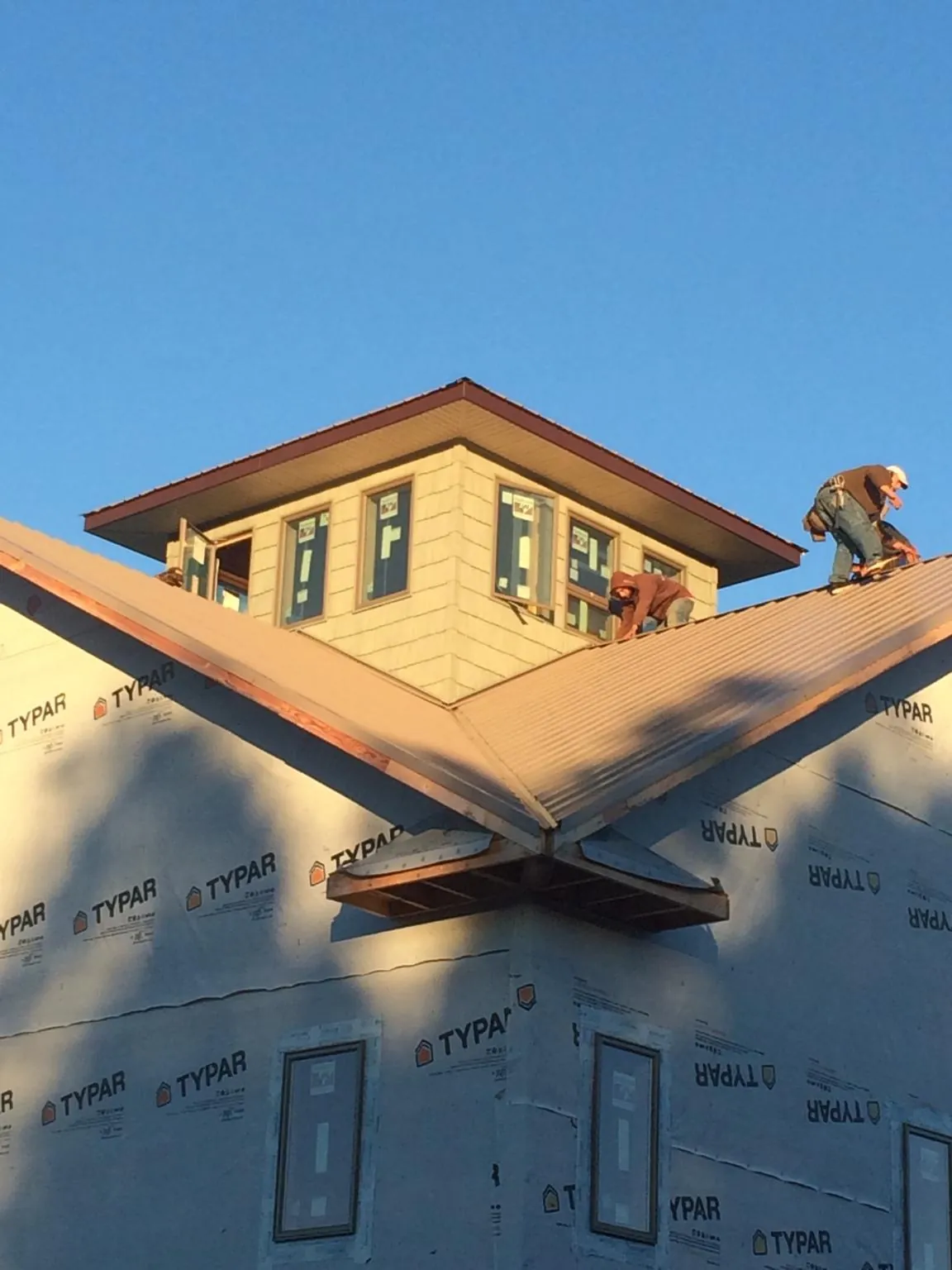 Roofers working around a rooftop cupola on a new metal roof at sunset — Roof Waterproofing in Oostburg by Roofing Brothers